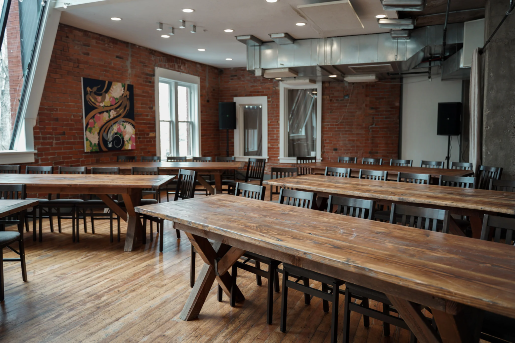 Spacious Agora Room at Boulder Riverside with rustic farm tables, black chairs, exposed brick, and original artwork