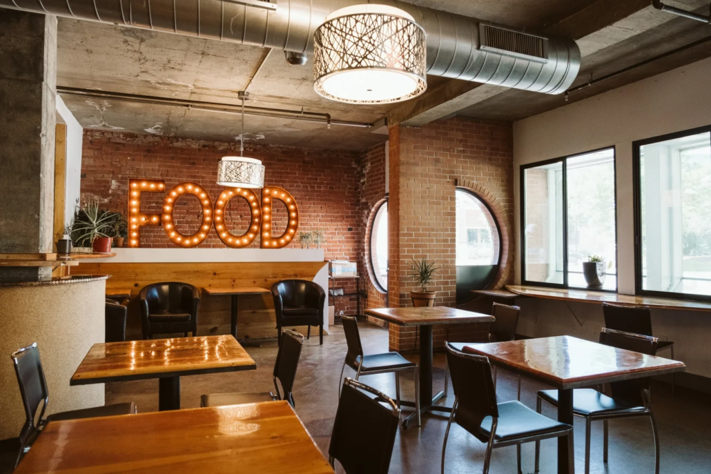The Café at Boulder Riverside featuring illuminated FOOD sign, exposed brick walls, and mixed seating.