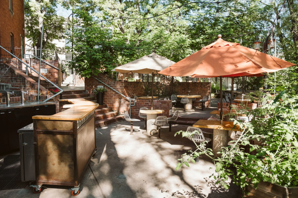 Sun-drenched outdoor patio at Boulder Riverside with orange umbrellas, greenery, and bar cart setup